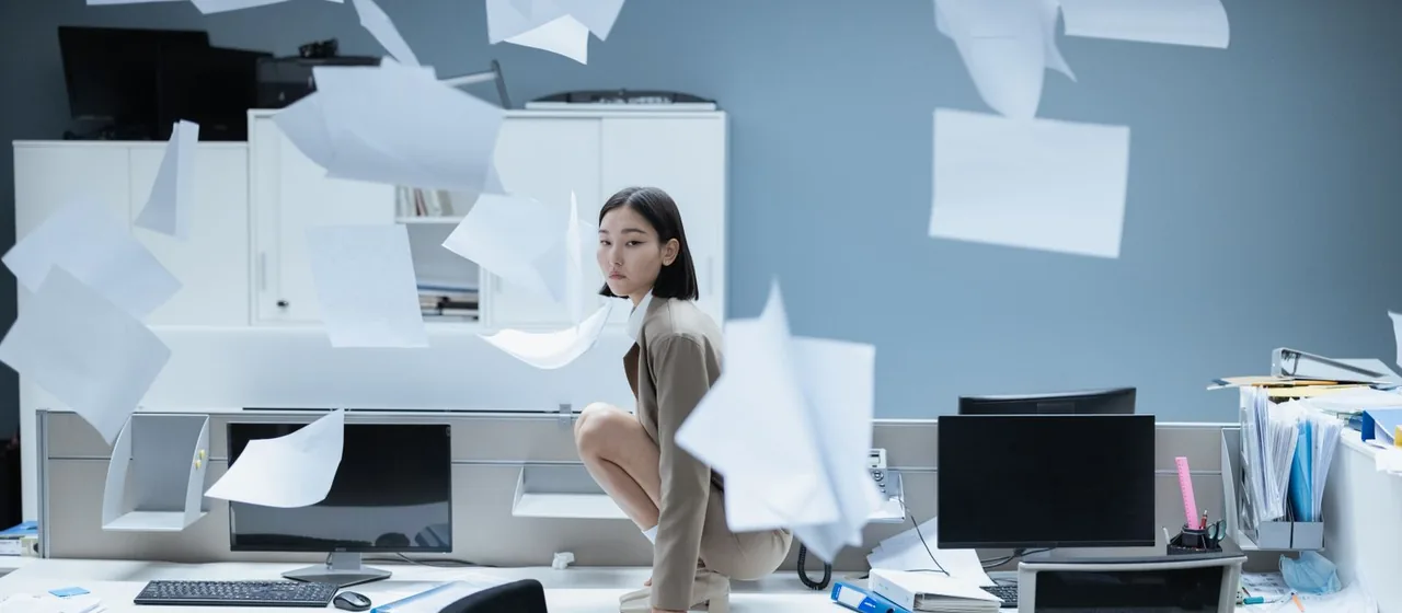 Vrouw te midden van rondvliegende papieren op een rommelig bureau