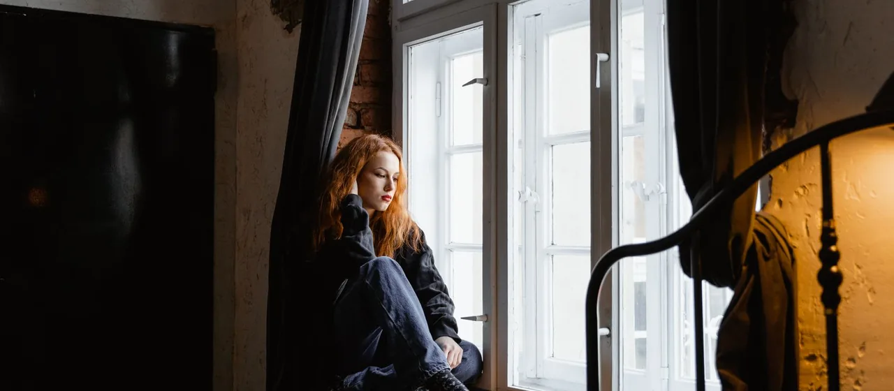 Vrouw zit peinzend bij het raam